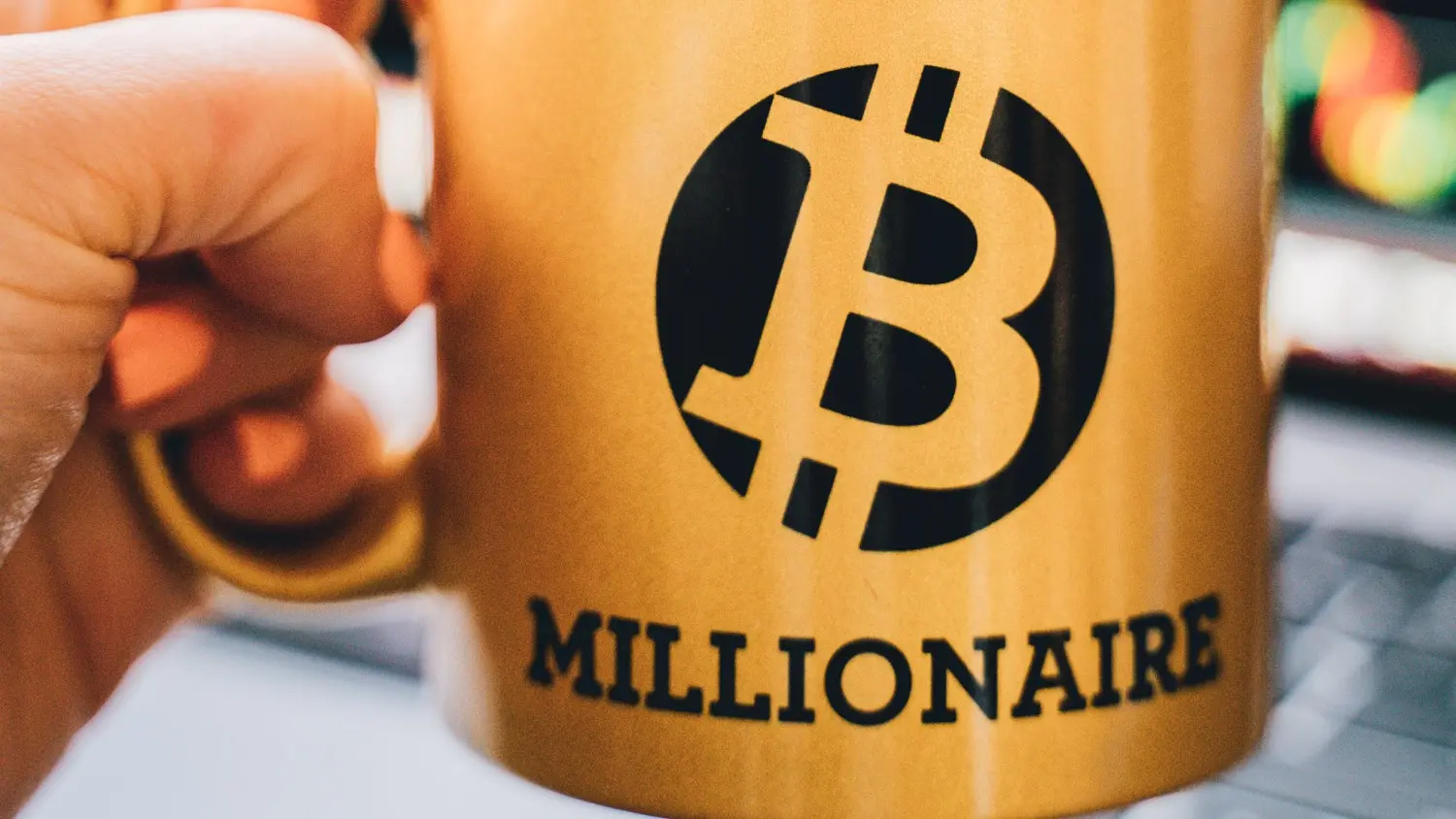 Une main tenant une tasse avec un symbole de Bitcoin et une mention millionnaire